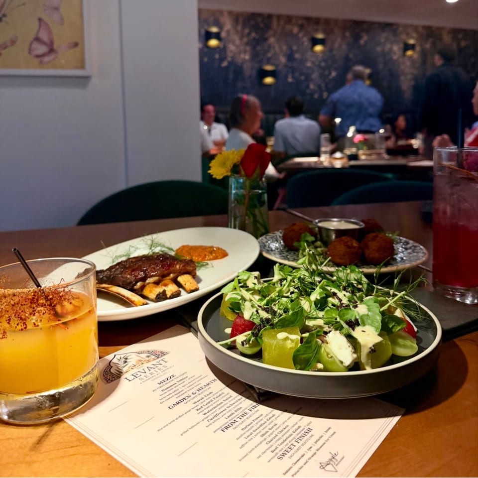 A table at Levant Series restaurant with lamb ribs, salad, falafel, cocktails, and a menu.