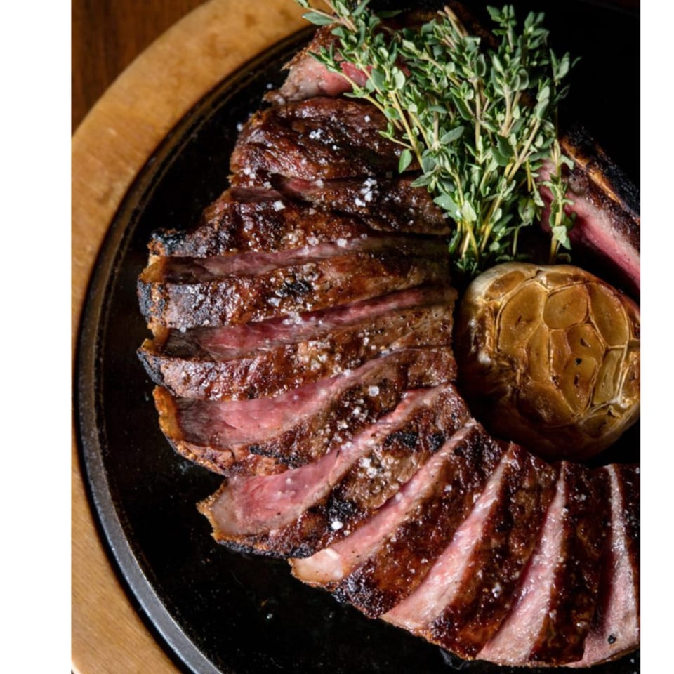 Sliced steak with fresh thyme and roasted garlic on a black plate at Argyle Restaurant.