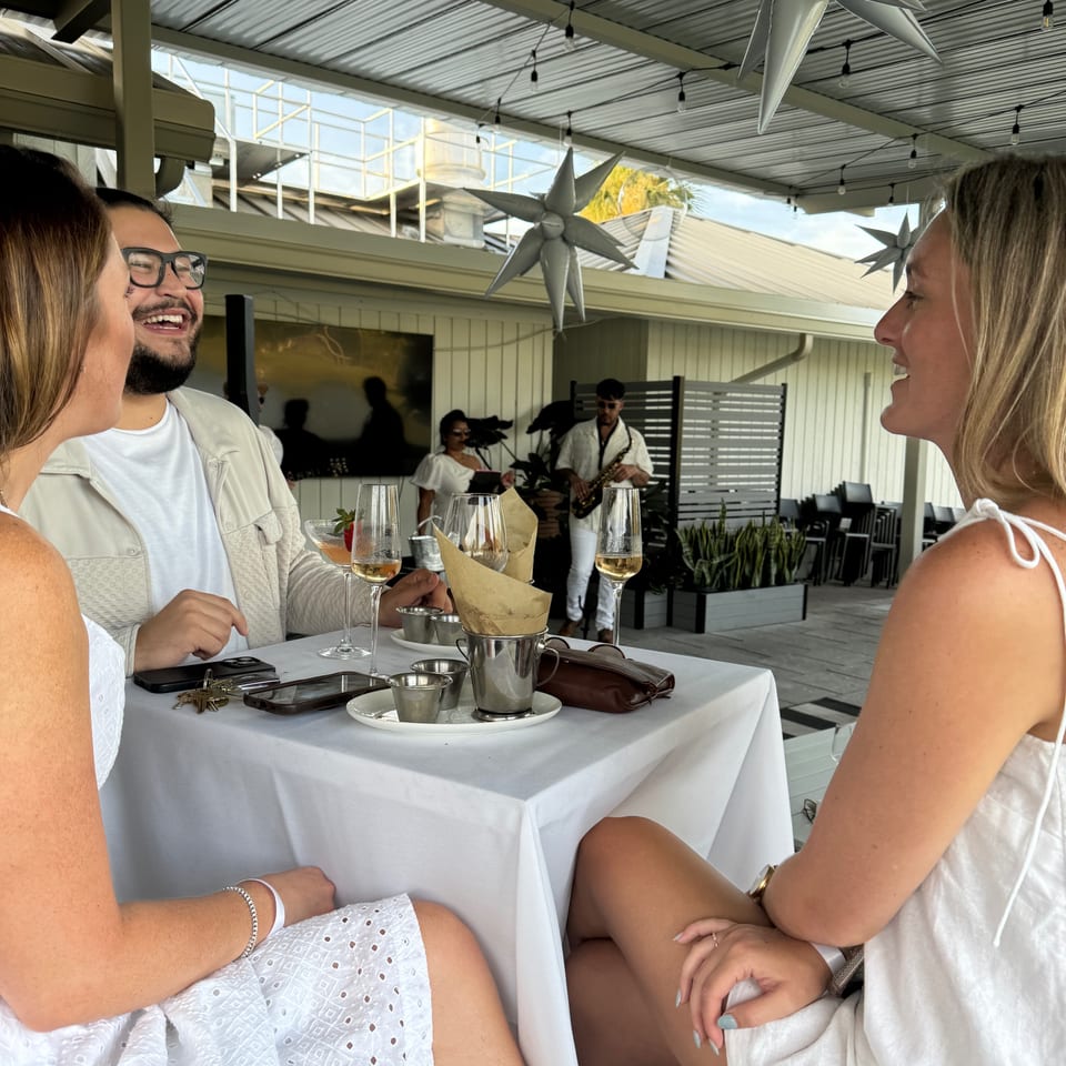 Three people enjoying drinks at an outdoor restaurant table with live music in the background.