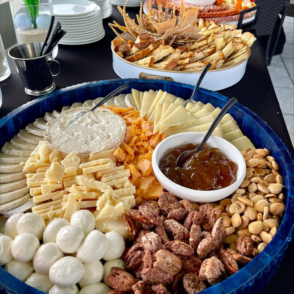 A large blue platter filled with various cheeses, nuts, and a bowl of fig jam.