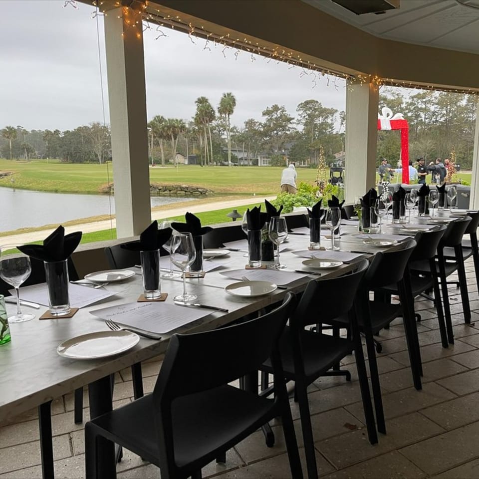 Long dining table set for guests on an outdoor patio overlooking a golf course and lake.