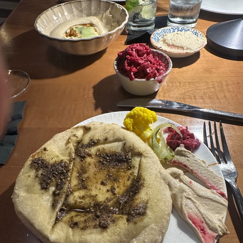 A Middle Eastern mezze spread with pita bread, hummus, beet salad, and pickled vegetables on a wooden table.
