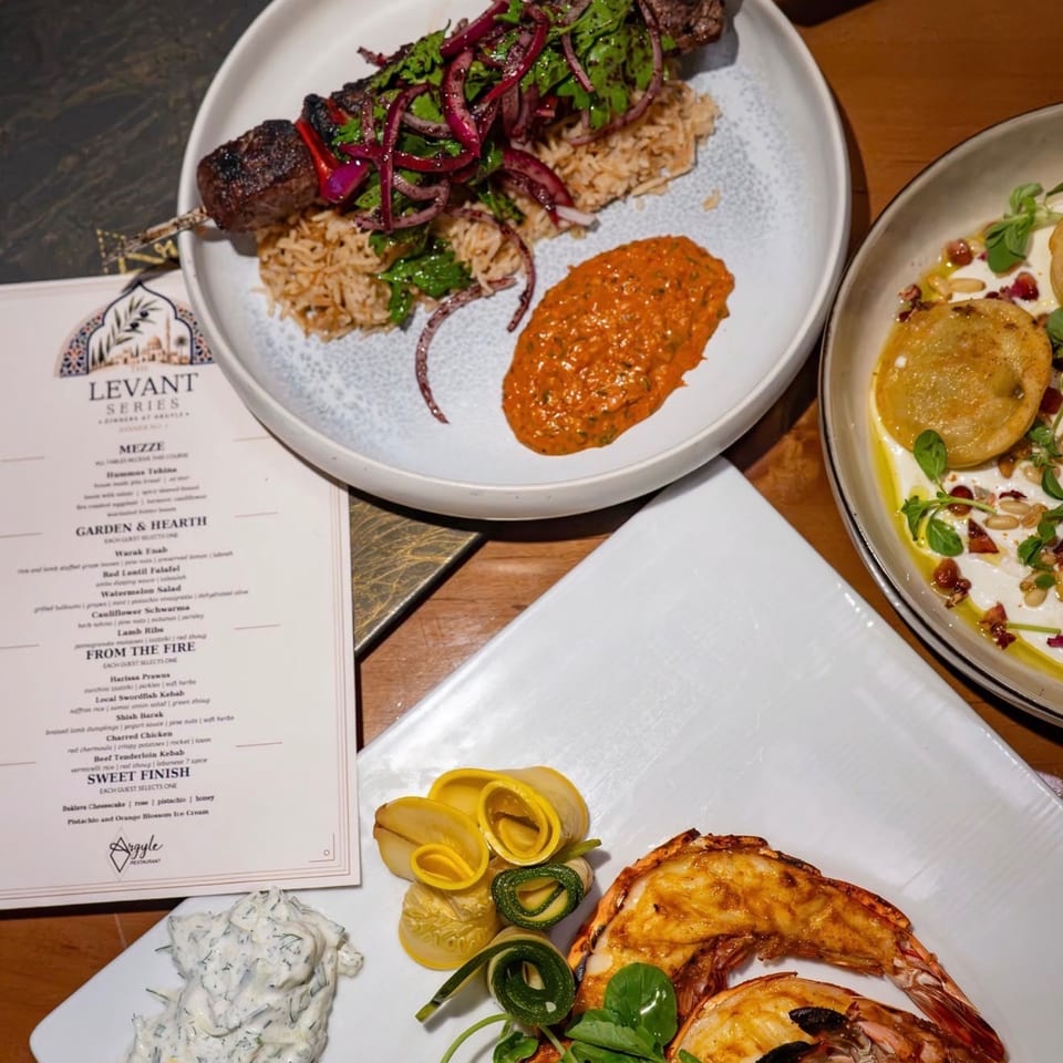 A table spread with Levant Series dishes: kebab, rice, sauce, shrimp, and a menu.