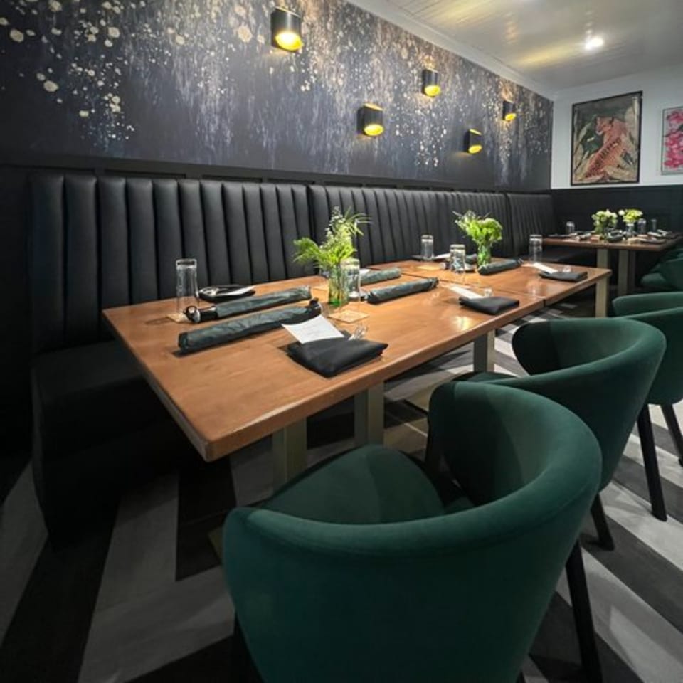 Argyle Restaurant dining room with long wooden tables, green chairs, and dark wall art with sconces.