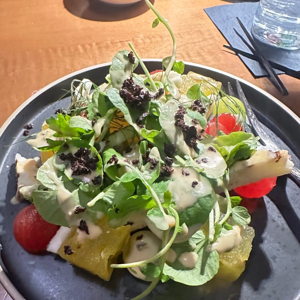 A vibrant salad with greens, cherry tomatoes, pineapple, and a creamy dressing on a dark plate.