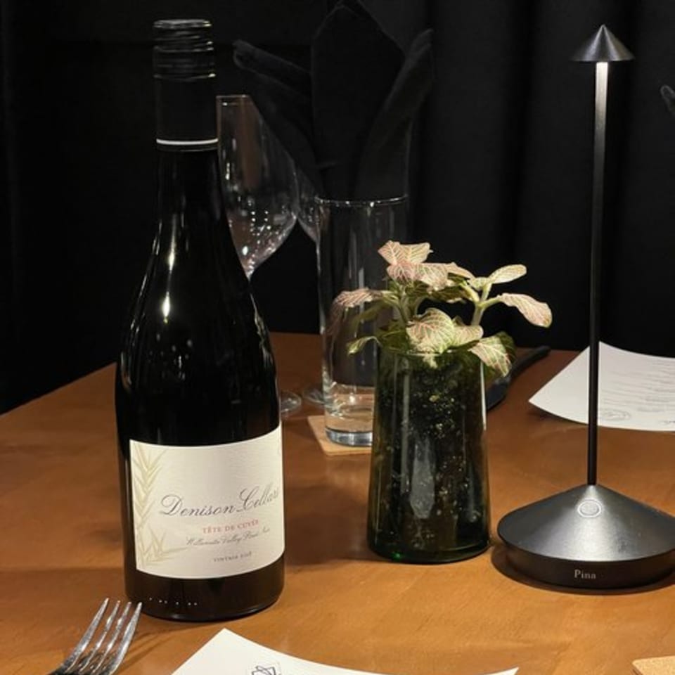 A bottle of Denison Cellars wine, a plant, and a modern table lamp on a wooden table.