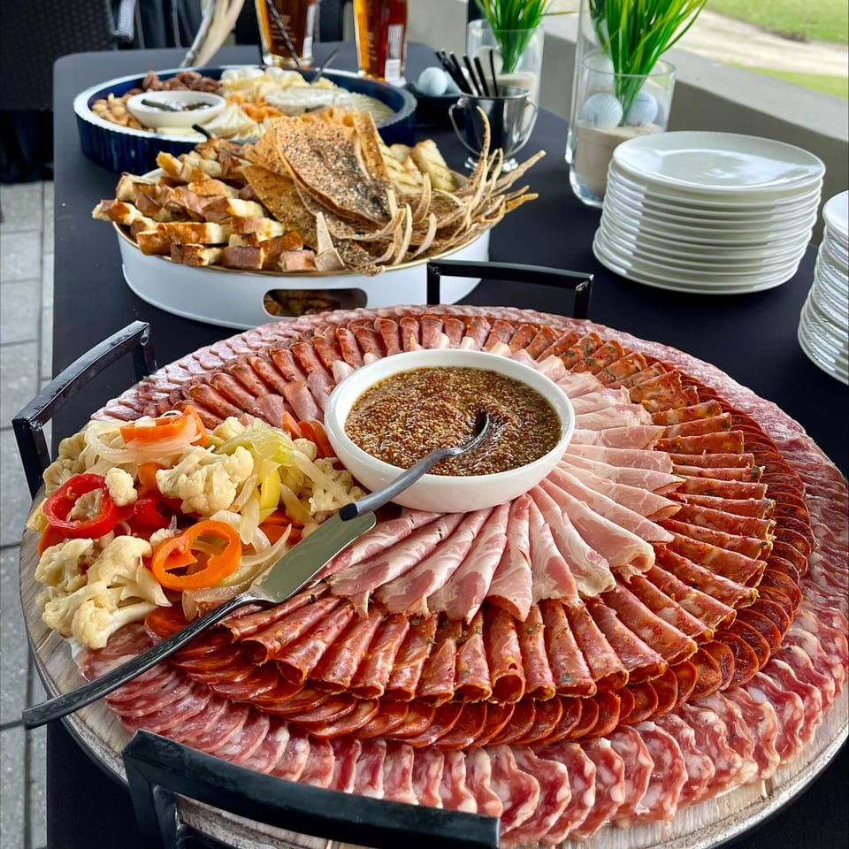 A large charcuterie board with various meats, pickled vegetables, and a bowl of mustard.